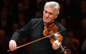 Violist Pinchas Zuckerman stands on stage while playing his instrument. Stern look on face, wearing glasses