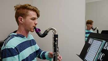 college student plays bass clarinet in a practice room