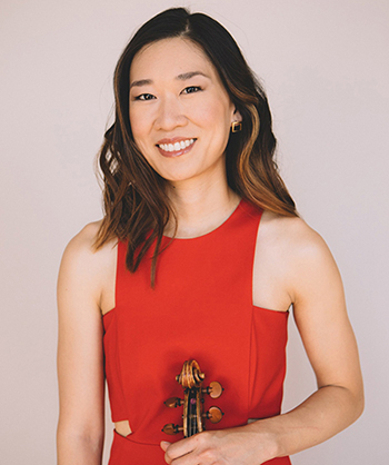 woman in red dress poses for photo, smiling with the top of a stringed instrument in her hand