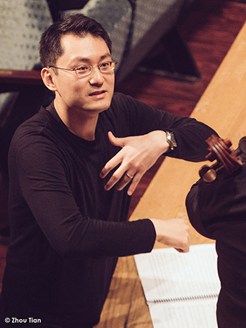 close up of man standing on the floor at the front of a state, pointing to sheet music and speaking to someone off camera