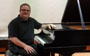 Rick Roe, jazz piano, sitting with one hand on the piano.