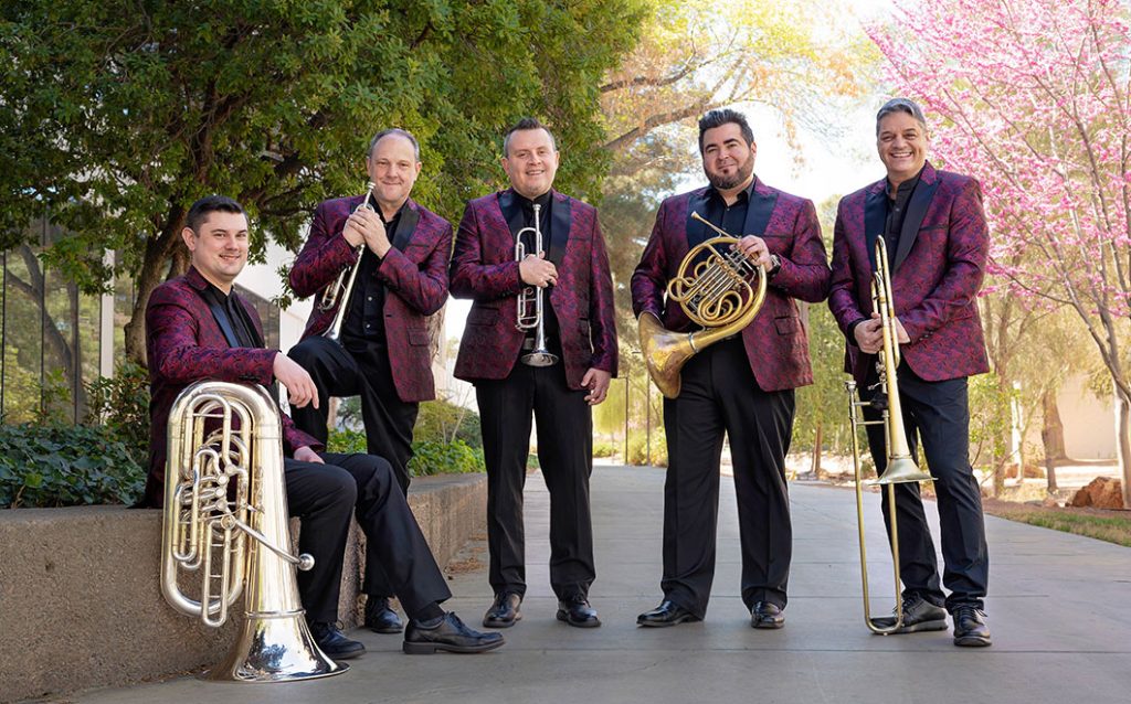 Boston Brass members standing outside in a park wearing colorful red sportcoats and all looking at the camera and smiling