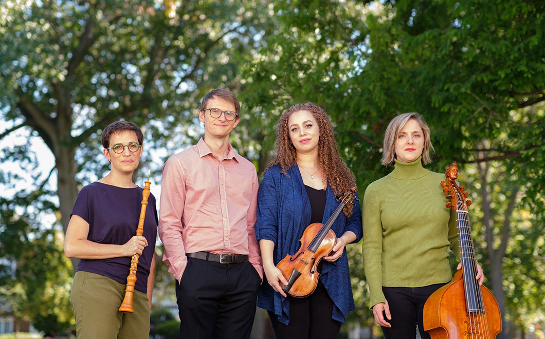 Photo portrait of Ensemble members: Debra Nagy, baroque oboe; Shelby Yamin, violin; Rebecca Landell, cello and viola da gamba, and Mark Edwards, harpsichord. Casual attire standing outside with greenery and trees in the background.