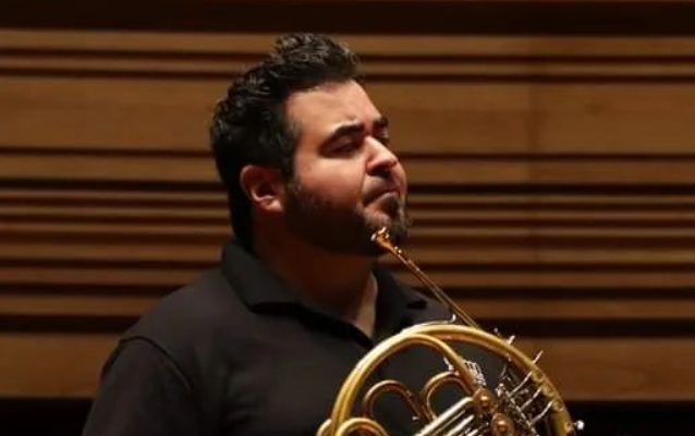 Chris Castellanos looks across a stage holding his horn