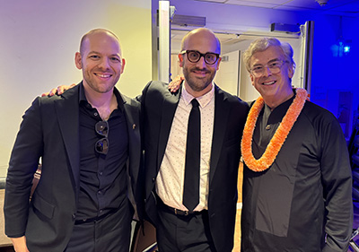 Three men stand with arms across shoulders, smiling.