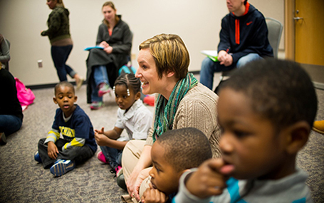 woman observes. smiles at and interacts with children at play in a class