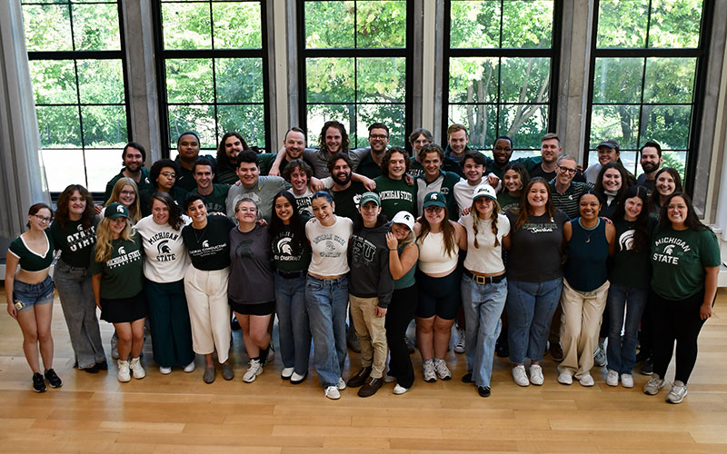 Male and female singers gathered for the ensemble photo of University Chorale, a large choral group of about 35 members. All wearing MSU Spartan attire