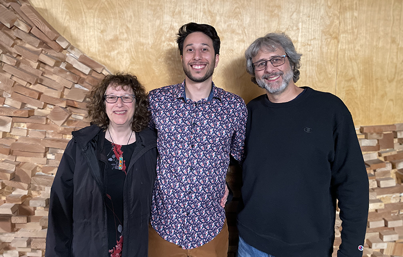 A mother (left) and father flank their adult son, all are smiling.