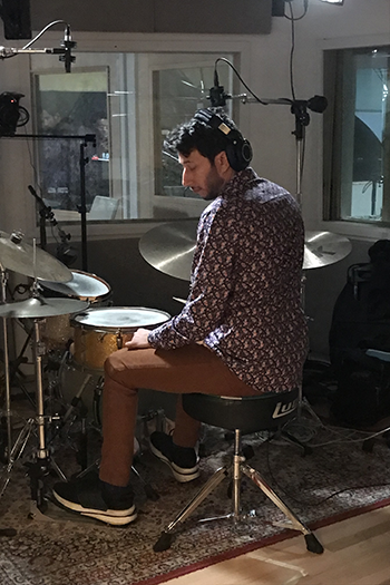 drummer plays in a studio setting, his back to the camera and head turned to the left.