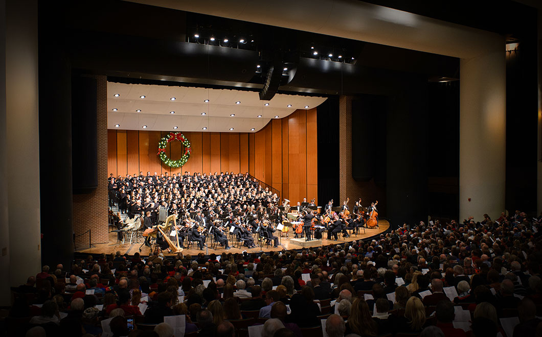 Cobb Great Hall Stage of Wharton Center with full risers accommodating 250 singers and a 50 member symphony orchestra. Large holiday wreath displayed in the background.