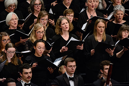 Group of choral singers, open song books and gestures to vocalize and express the lyrics