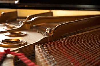 close view of the inside of a piano, gold steel and strings with red fabric on the ends.