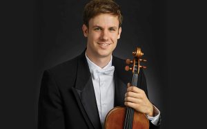 Portrait of Wesley Colllins, viola, smiling and looking at camera, holding viola and wearing a tuxedo