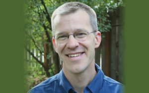 Portrait, Nathan Platte, smiling and looking at camera, wearing blue shirt and glasses