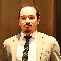 person with dark hair and goatee wearing tan sport coat and dark tie