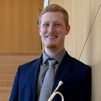 person in blue suit and tie, mouthpiece of a trumpet in bottom of image