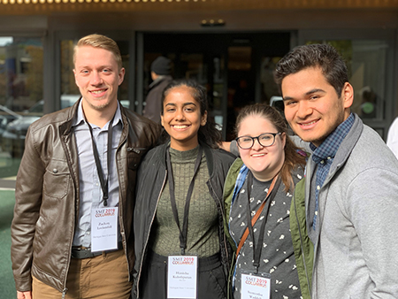 Four people standing close together, each has a lanyard with badge attached.