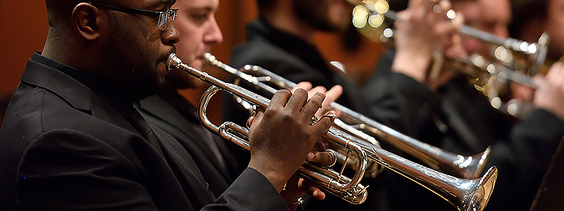 side view of people playing trumpets while dressed in formal black concert attire.