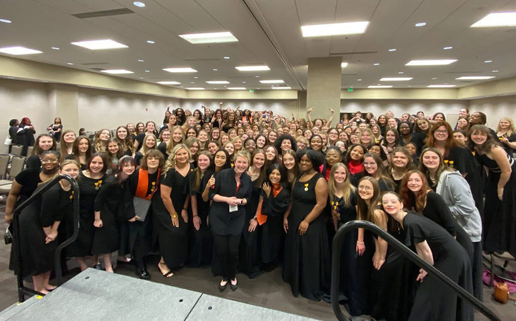 a large group of people smile while gathering together for a group photo; all wearing black