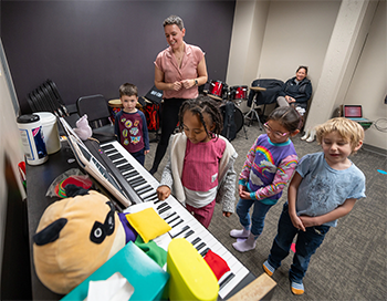 Four children and two adults in a room with an electronic keyboard instrument and a few toys.