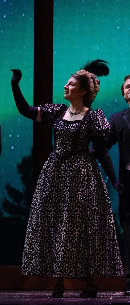 person wearing long formal gown with feathered headpiece raises arm