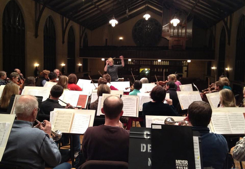a large musical band and singers on a stage led by a conductor