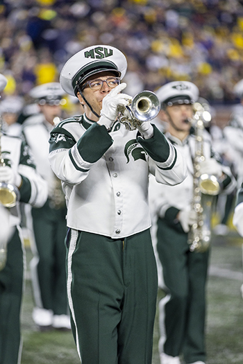 person in green and white marching band uniform plays trumpet.