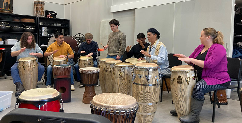 a group of seven people play percussion instruments in a rehearsal room