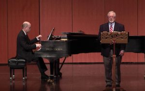 Professor Richard Fracker singing in the crook of the piano. Elden Little playing at the piano.