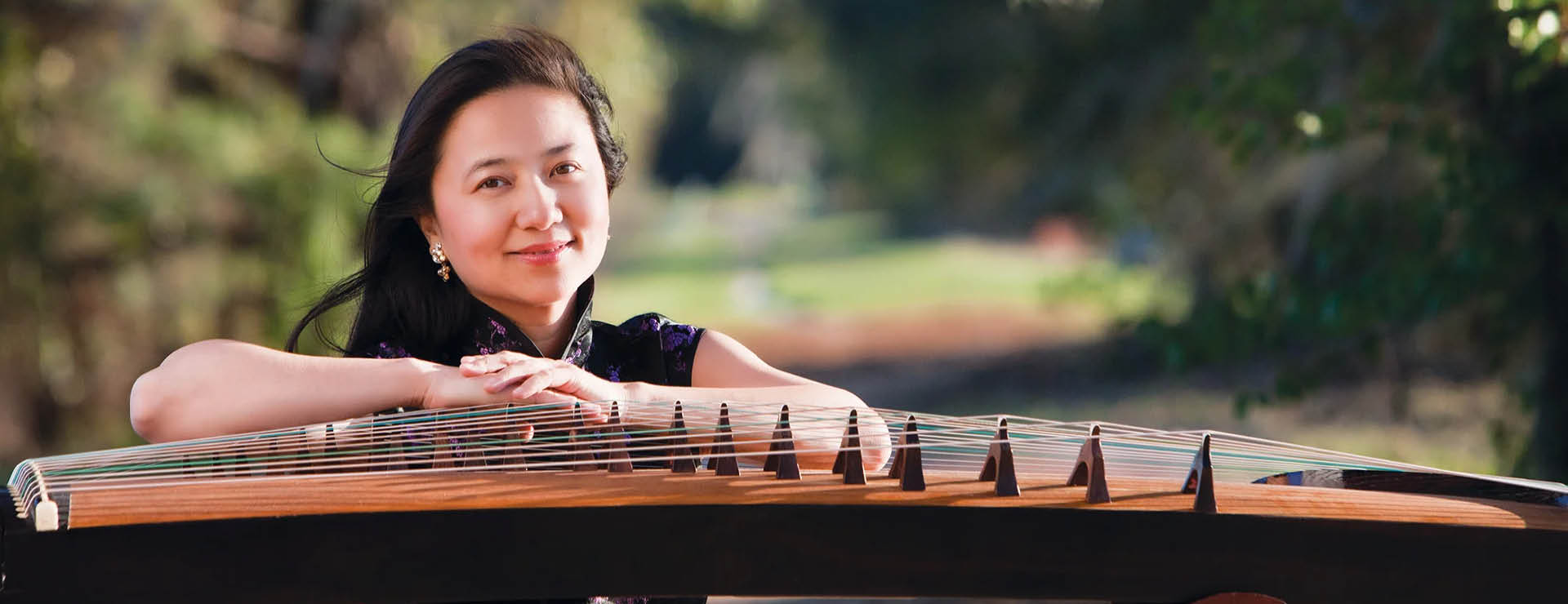 Image of guest artist Dr. Haiqiong Deng next to a traditional Chinese instrument - Zheng