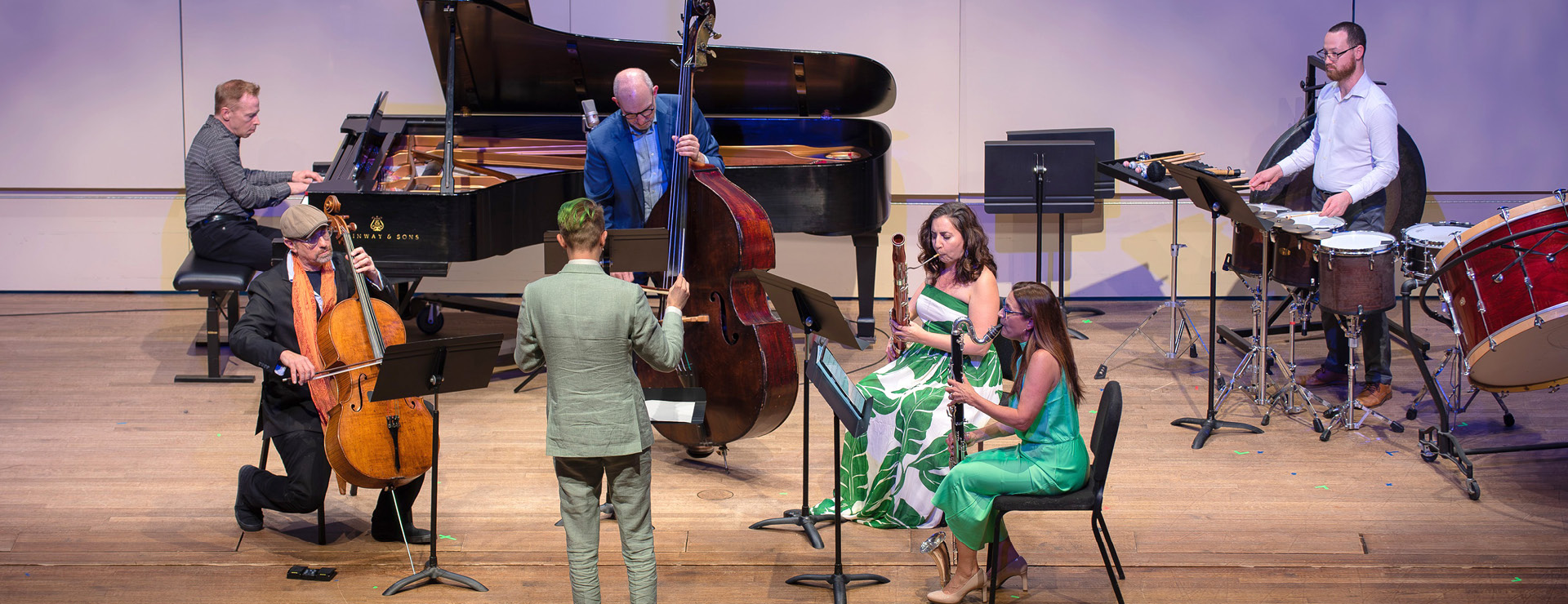 American Modern Ensemble musicians performing on stage, dramatic lighting with conductor directing a pianist, cellist, bassist, bassoonist, clarinetist and percussionist.
