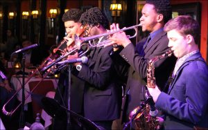 Jazz musicians standing and performing in concert hall, wearing formal attire