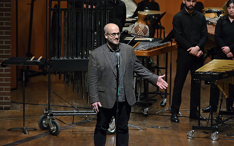 person on stage speaking with musicians in background
