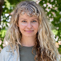 portrait of Christian Gibson, closed lip smile, looking at camera with green tree leaves in the background