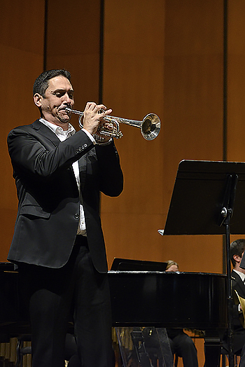 person on stage in dark suit playing trumpet