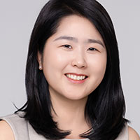 Portrait: Hae Won Jang, smiling and looking at camera, gray background