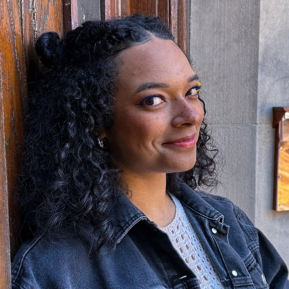 person in blue jean jacket smiling, leaning against wooden door