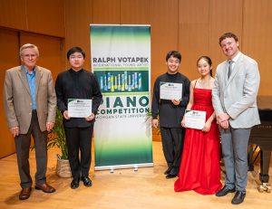 Group photo of pianists holding up their awards for the piano competition. Banner on stage with directors and competition namesake 
