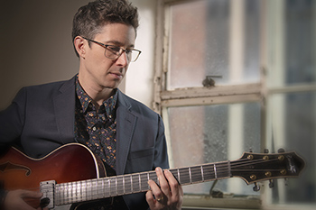 person in gray suit playing an electric guitar