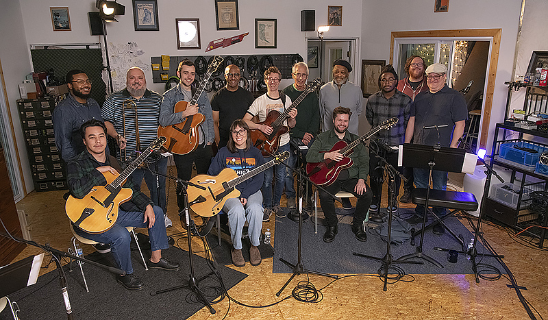 large group of musicians in a studio holding instruments and smiling