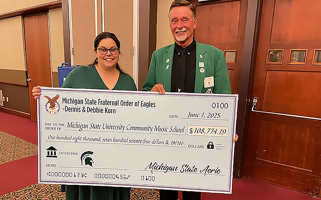 two people wearing green smile as they hold a large check in front of them