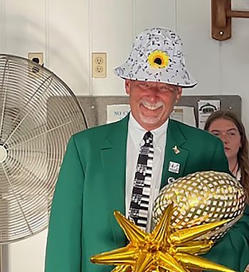 a person laughs while wearing a green coat, sparkling hat, and holding items