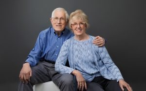 two people seated side by side in photo studio, leaning on one another
