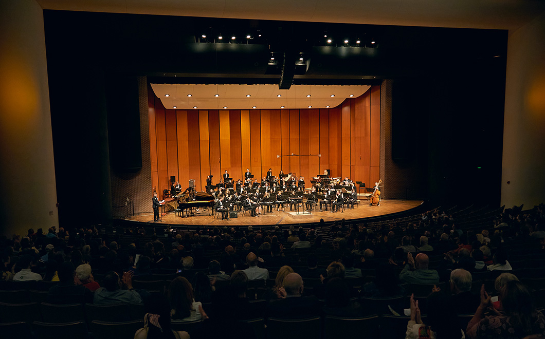 from the back of a large performance hall, a wind symphony is performing on a stage