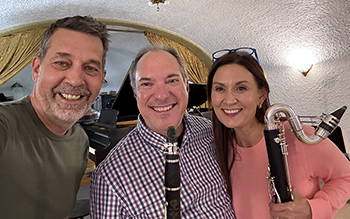 three people smiling close together, two holding clarinets