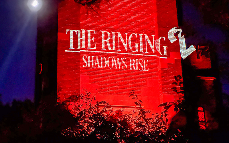 the side of a tower is lit orange with writing in white that reads The Ringing 2: Shadows Rise