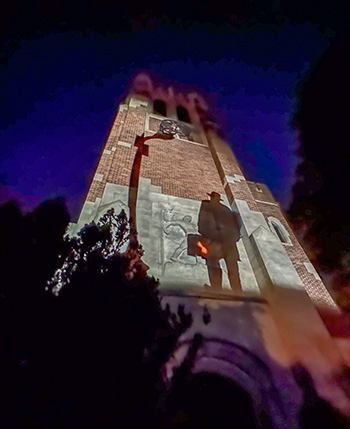 a tower lit up by lights that project the silouhette of a man in a hat
