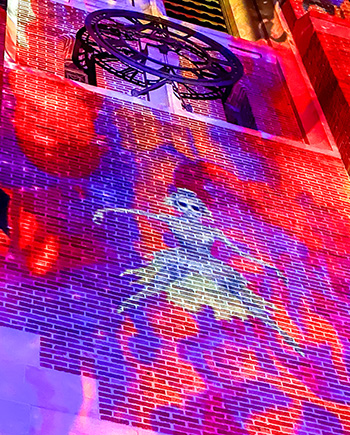 a bricked building lit up by lights that project the figure of a spooky girl
