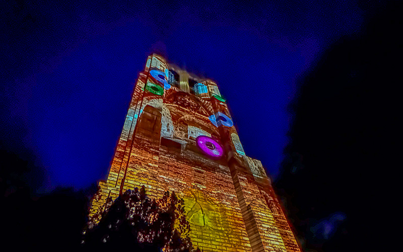 a tower lit up by lights that look like colorful clockwork pieces