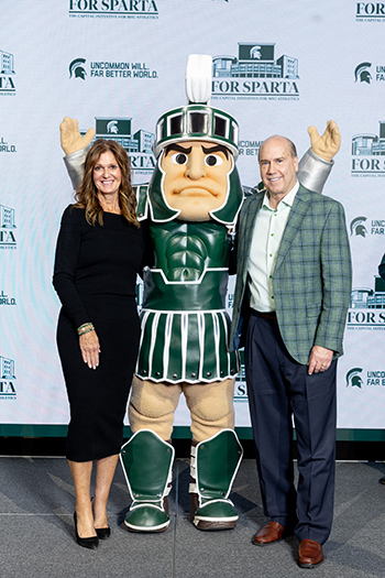 two people stand on either side of MSU mascot Sparty